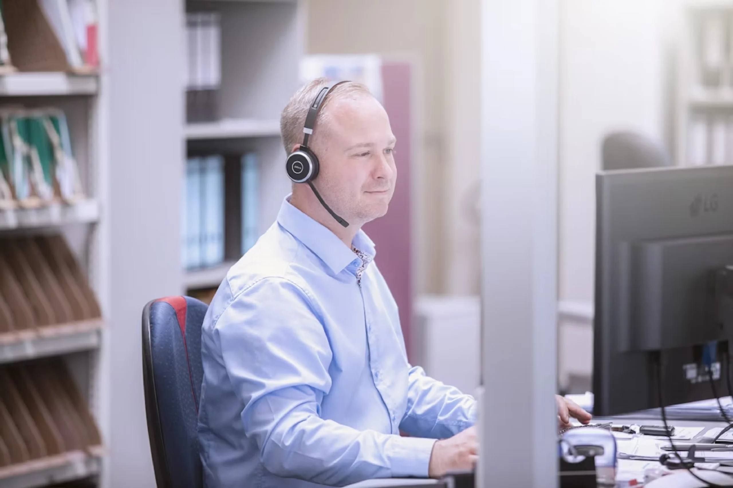 Ansprechpartner sitzt mit einem Headset, mit Mikrofon vor einem Pc