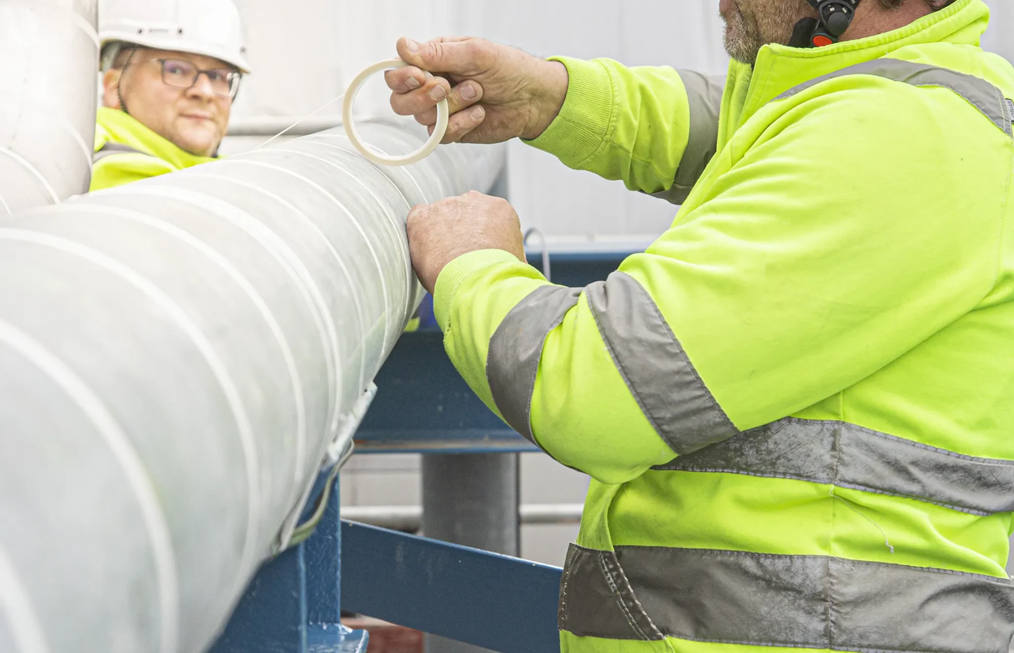 Mann in Neon Artbeitsjacke taped ein Rohr