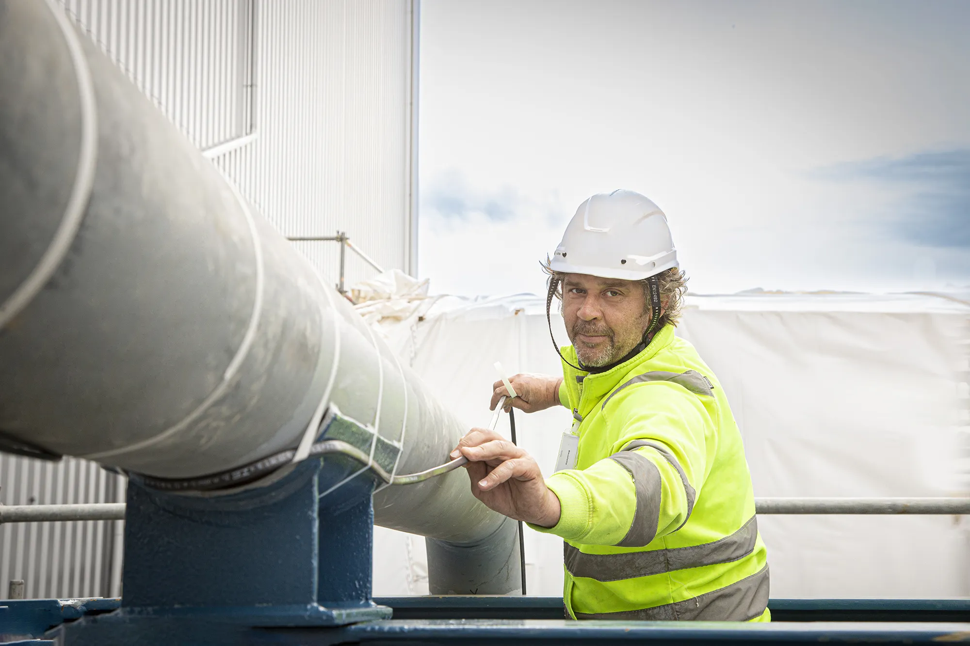 Ein Mann mit Helm verlegt ein Heizband an einem dicken Rohr